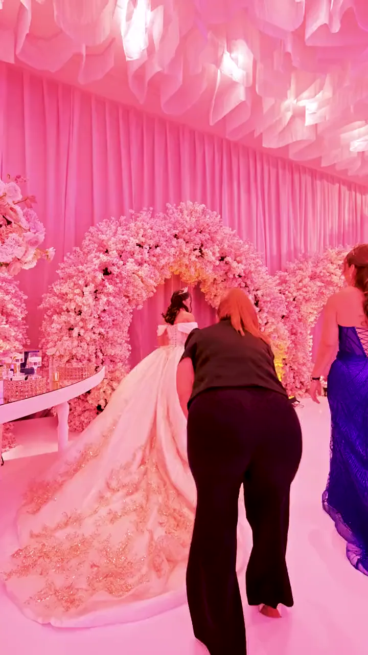Alguien del equipo acomoda el vestido de la quinceañera en un salón entelado en rosa